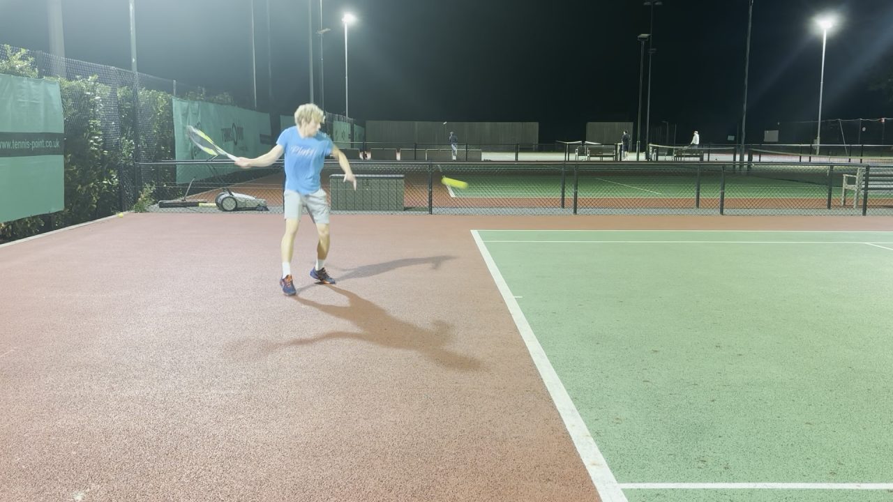 A floodlit court filmed side-on with the phone sideways: the whole body in shot, with room around the racket.